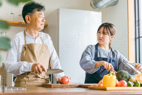 家のキッチンで怒るアジア人高齢者男性と若い女性（家政婦・家事代行） 
