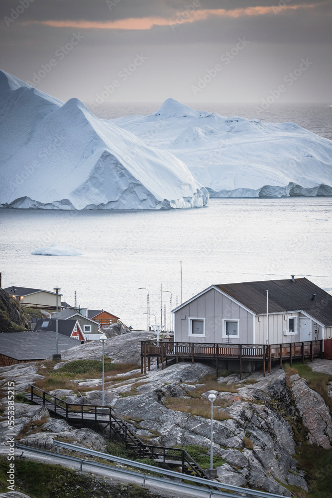 Casas de madera de colores en pueblo costero con icebergs flotando de fondo.