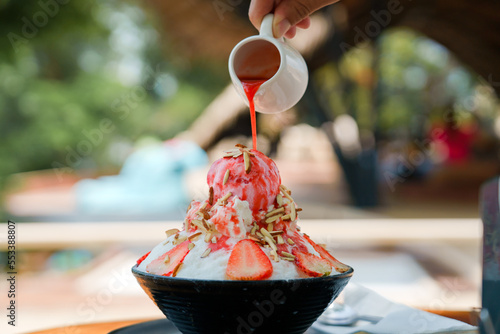 Japanese shaved ice dessert , Hand pouring sweet strawberry sauce on ice cream. Served with strawberry kakigori bingsu topped with almond stick condensed milk. Traditional summer dessert in Japan.