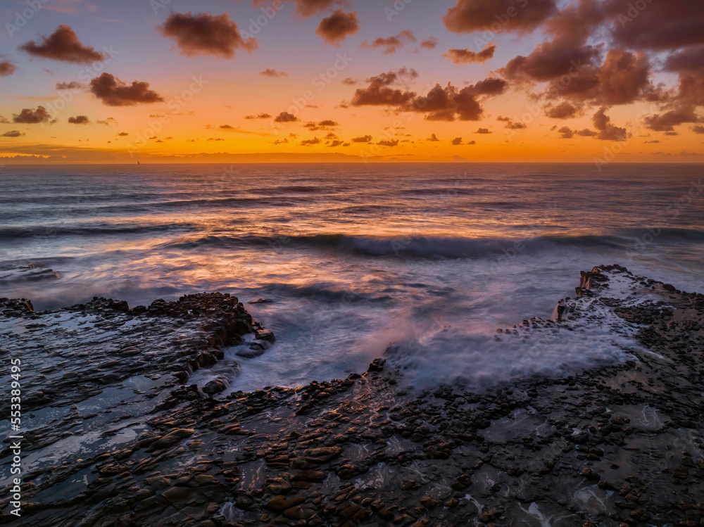 Fototapeta premium Surfs up sunrise at the seaside with scattered clouds