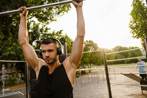 Young muscular man doing pull ups on horizontal bar outdoors on sports ground © Drobot Dean