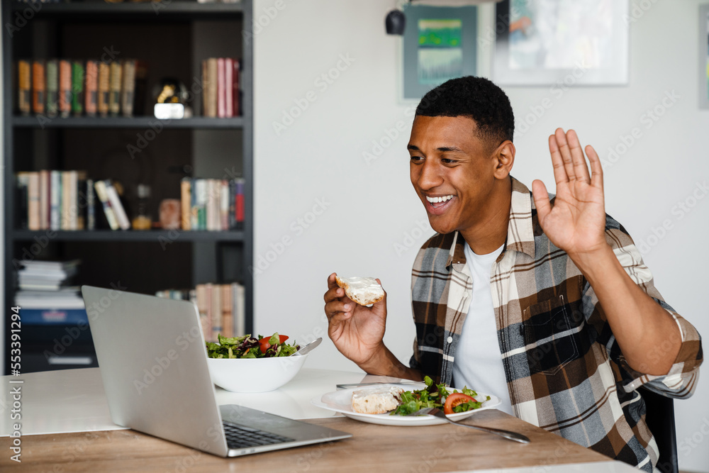 Young african man having video call via laptop while having lunch at home Young african man having video call via laptop while having lunch at home