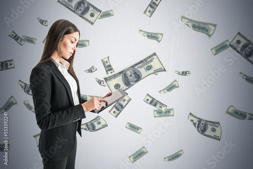 Attractive young european businesswoman using mobile phone with creative dollar bill rain on concrete wall background. Millionaire, rich and cash concept.