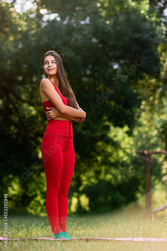 Beautiful fit young girl in red sportswear doing stretching exercises outdoor