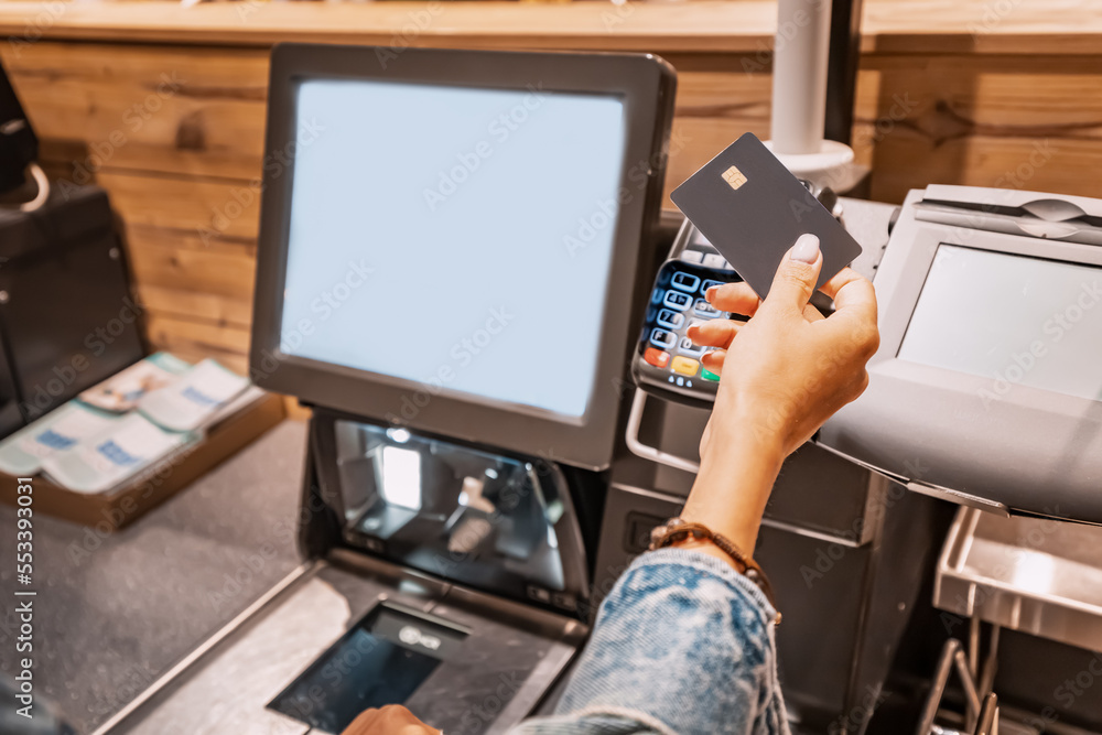 The girl buyer applies a credit card to the pos terminal to pay for purchases at the self-service checkout