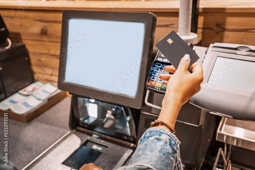 Obraz na płótnie The girl buyer applies a credit card to the pos terminal to pay for purchases at the self-service checkout w salonie