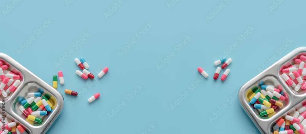 Above view of Colorful antibiotic capsule pills on tray and blue background. Antibiotic drug resistance. Antimicrobial drugs. Prescription drugs. Pharmaceutical industry. Health care and medicine.