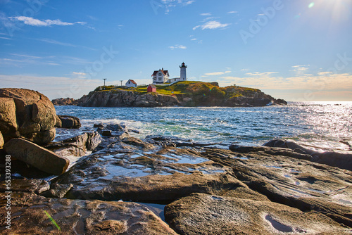 Rocky Maine coast with ocean and island featuring lighthouse with blue sky