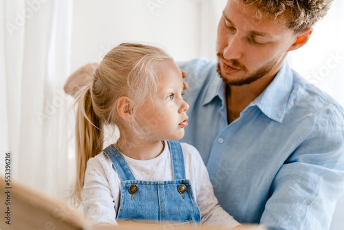 Young white father and little daughter reading book together at home © Drobot Dean