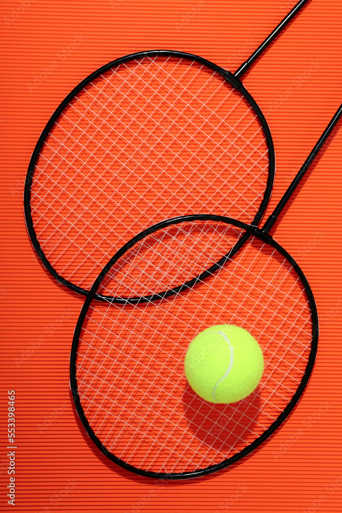 Badminton rackets and tennis ball on textured orange background