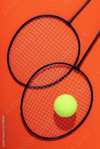 Badminton rackets and tennis ball on textured orange background © Atlas