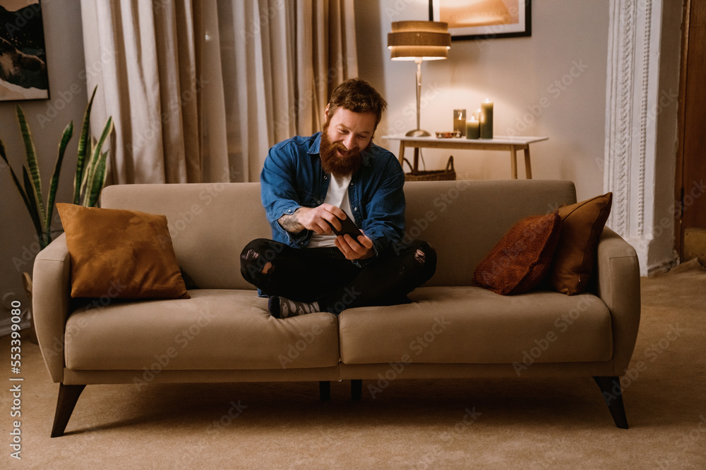 Excited man playing game on mobile phone while sitting on sofa at home Excited man playing game on mobile phone while sitting on sofa at home
