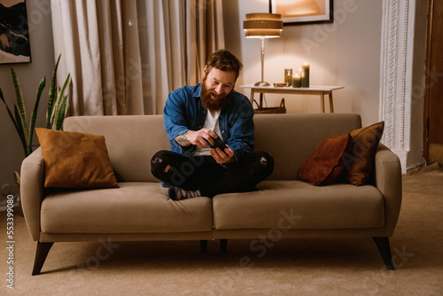Excited man playing game on mobile phone while sitting on sofa at home © Drobot Dean