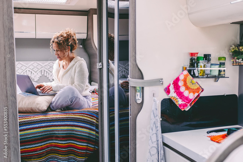 Alternative office workplace concept. Woman working on laptop in camper van bedroom. Van life and smart travel working life. Female people in modern job computer activity alone sitting on bed