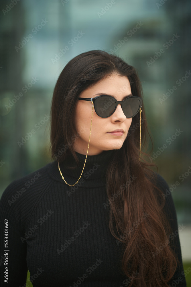 Businesswoman in the city. A stylish and attractive caucasian lady wears fashionable dark sunglasses with chain accessories. Outdoor portrait of a confident woman. Businesswoman in the city. A stylish and attractive caucasian lady wears fashionable dark sunglasses with chain accessories. Outdoor portrait of a confident woman.