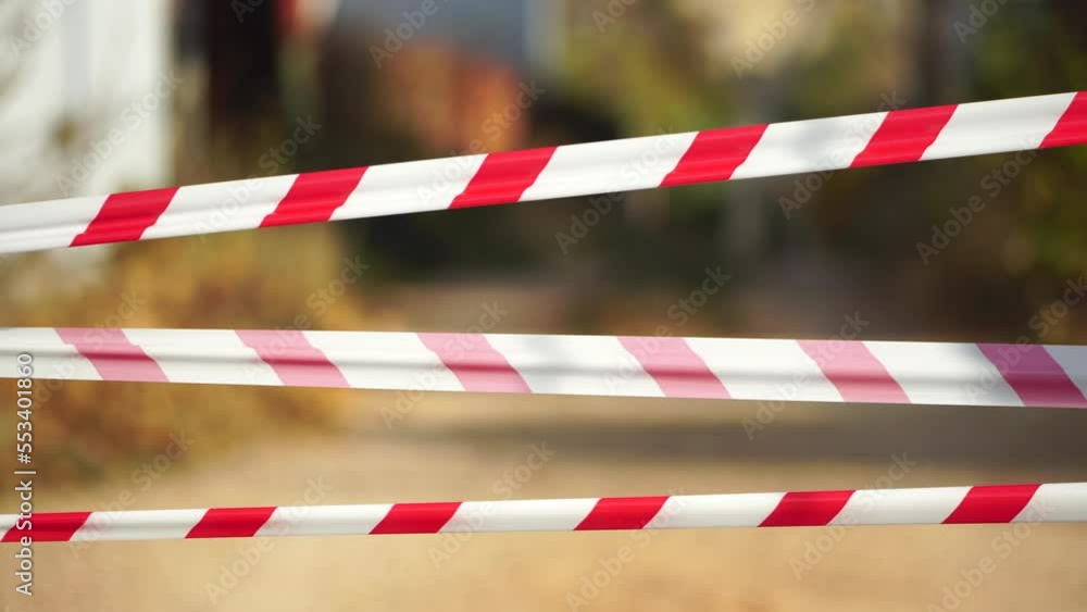 Red and white warning tape swinging in the wind. Protection sign. Don't cross the line. Red White caution tape pole fencing is protects for No entry. Backdrop without people, empty street. Red and white warning tape swinging in the wind. Protection sign. Don't cross the line. Red White caution tape pole fencing is protects for No entry. Backdrop without people, empty street.