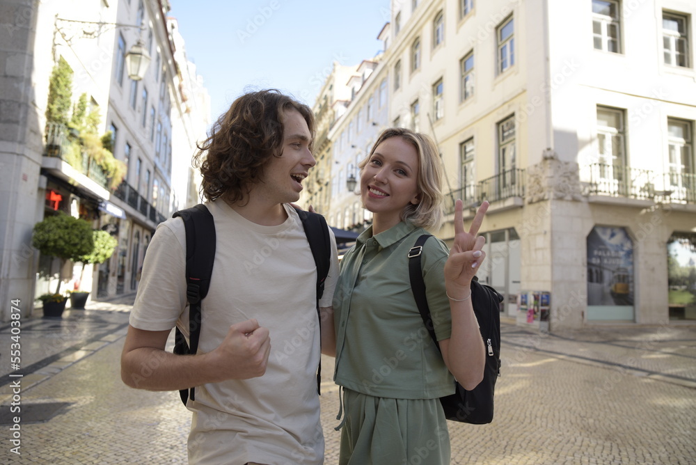 Fototapeta premium Happy tourist couple walking. Man and woman travelling, talking, woman showing peace sign. Portrait, travelling concept