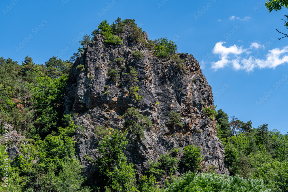rocher avec sa falaise a pic recouvert d'arbres verts proche de Courgoul dans le puy de dôme par une belle journée d'été