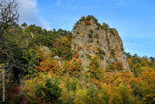 rocher avec sa falaise recouvert d'arbres coloré de jaune et d’orange par une journée automnale dans la vallée de Courgoul dans le puy de dôme