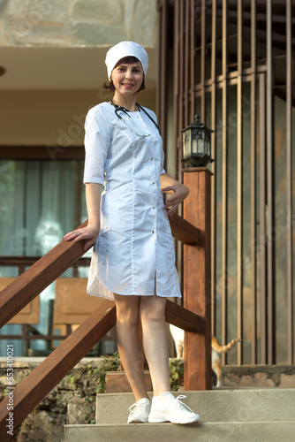 A nurse in a white coat and hat stands near the entrance to the hospital.
