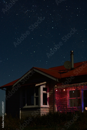 Milky Way Galaxy and Southern Cross constellation rising above red-roofed farmhouse in rural New Zealand. Billions of sparkling stars in the night sky of Southern Hemisphere photo