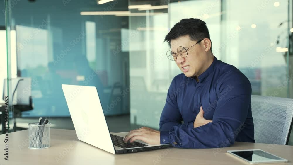 Unhealthy businessman IT programmer with heart attack holding chest suffers from severe pain at modern workplace Employee having cardiac medical health problem sitting at desk in the office indoors Unhealthy businessman IT programmer with heart attack holding chest suffers from severe pain at modern workplace Employee having cardiac medical health problem sitting at desk in the office indoors