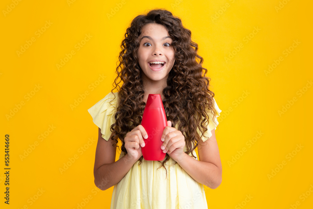 Teen child girl with shampoo bottle or shower gel isolated on yellow background. Kids hair cosmetic product. Excited teenager, glad amazed and overjoyed emotions. Teen child girl with shampoo bottle or shower gel isolated on yellow background. Kids hair cosmetic product. Excited teenager, glad amazed and overjoyed emotions.