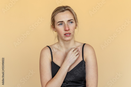 Portrait of the thoughtful upset woman standing over beige background  lost in thoughts. Pensive unhappy girl feeling lonely and depressed  thinking about relationship or personal problems