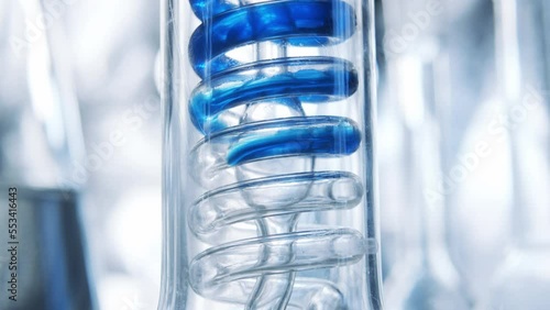 Blue fluidity flows through spiral pipe. Glass big test tube.  Laboratory experience and research. cleaning process. Production of cosmetics and perfumes. Liquid purification in the laboratory. 