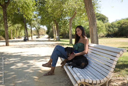 Young woman, brunette, slender, dressed in green t-shirt and jeans, sitting on a bench next to her dog, happy and in a loving attitude. Concept animals, pets, friends, love, dogs, breed.