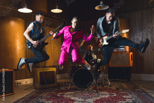 Full-length indoor shot of music band jumping. Lead singer and two guitarist jump in the air. Recording studio or garage studio interior. High quality photo