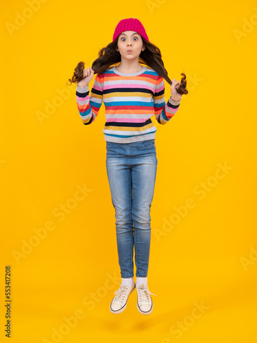 Amazed teenager. Jump and run. Fashion happy young woman in knitted hat and sweater having fun over colorful blue background Excited teen girl.
