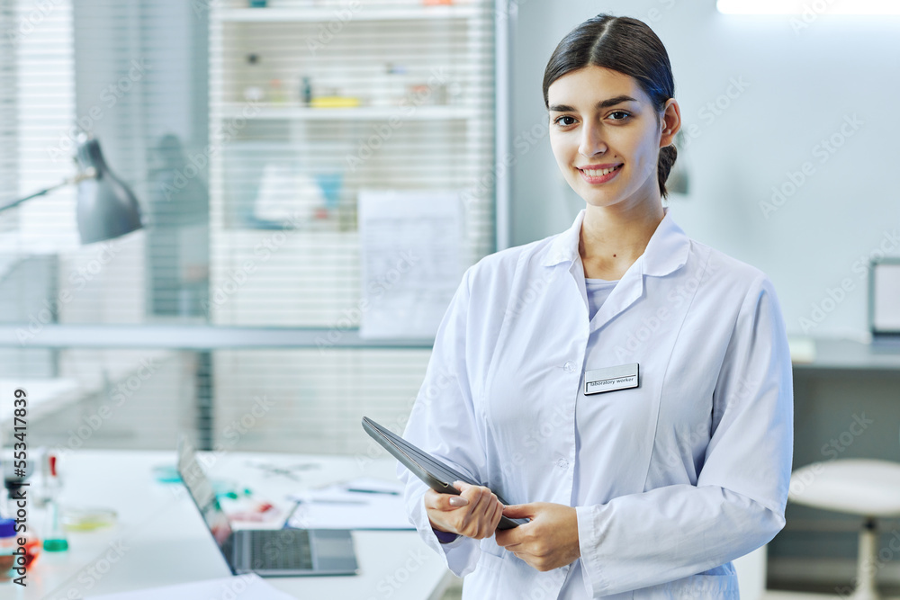 Waist up portrait of smiling Middle Eastern woman standing in medical laboratory, copy space Waist up portrait of smiling Middle Eastern woman standing in medical laboratory, copy space