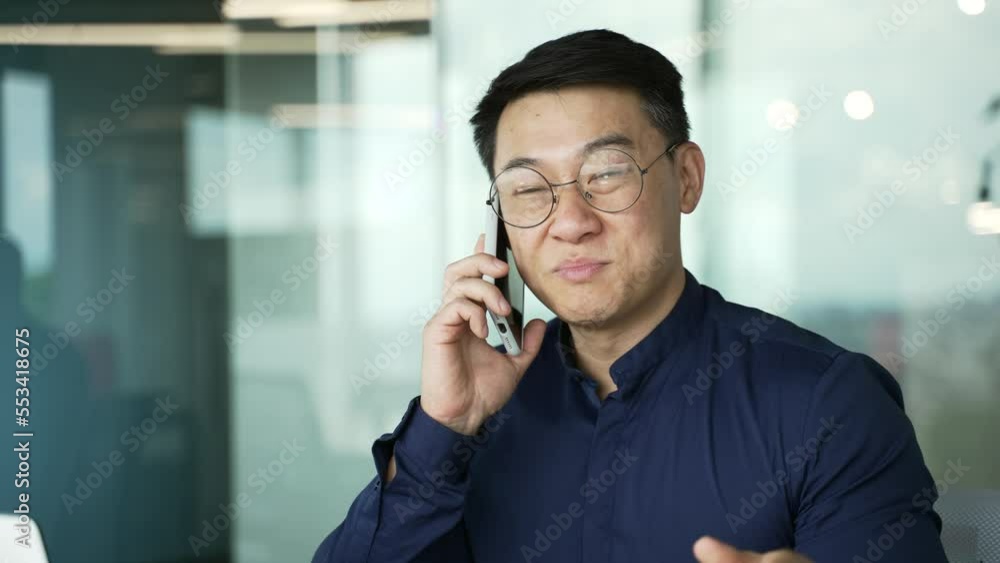 Confident asian businessman IT programmer with glasses talking on mobile phone at modern office indoors Successful office worker male having professional conversation chat on smartphone at workplace Confident asian businessman IT programmer with glasses talking on mobile phone at modern office indoors Successful office worker male having professional conversation chat on smartphone at workplace