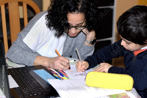 Photograph of a young mother tutoring and helping her son with his school homework. Selective focus photography. Photograph with space for copy space