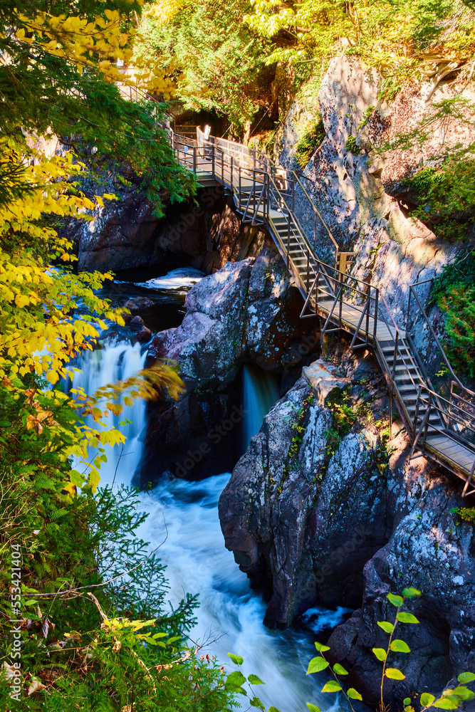 Fototapeta premium Boardwalk steps built into rocky cliffs of deep gorge with rapids, waterfalls, and fall colors