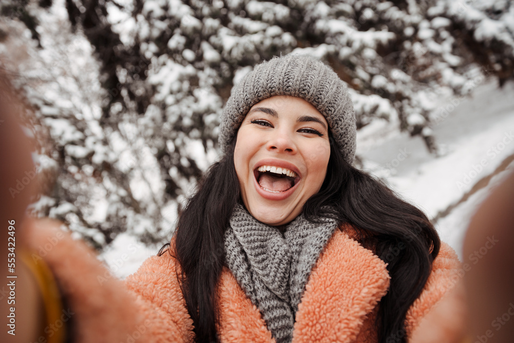Pretty happy woman in gray hat and pink coat takes selfie and play the ape in winter cold day. Girl takes winter selfie Pretty happy woman in gray hat and pink coat takes selfie and play the ape in winter cold day. Girl takes winter selfie