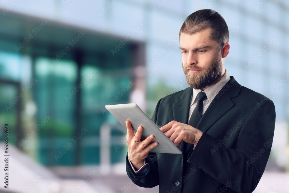 Fototapeta premium Rich business man standing outdoors and using digital table