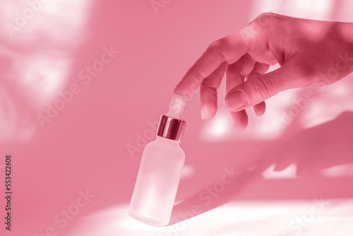 Natural cosmetics for body care. The hand touches a cosmetic bottle with essential oil or serum. White cosmetic bottle and female hand on a white background with shadows © Анастасія Шатирова