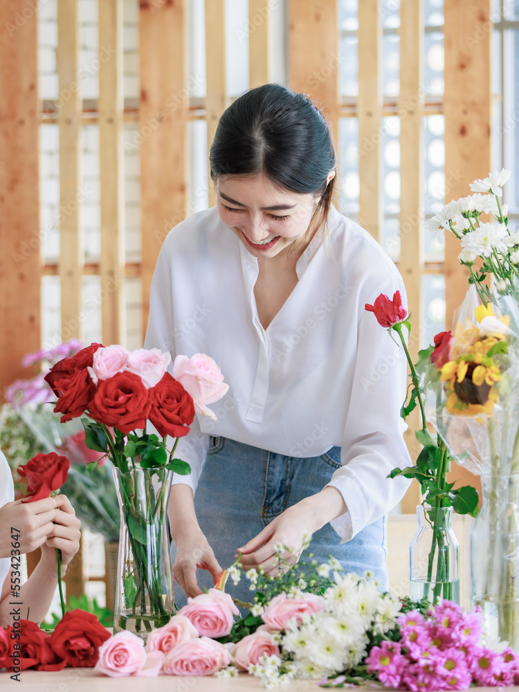 Millennial Asian young beautiful professional female flower shopkeeper decorator florist worker smiling holding flower bunch bouquet colleague arranging decorating stalk in floral store. Millennial Asian young beautiful professional female flower shopkeeper decorator florist worker smiling holding flower bunch bouquet colleague arranging decorating stalk in floral store.