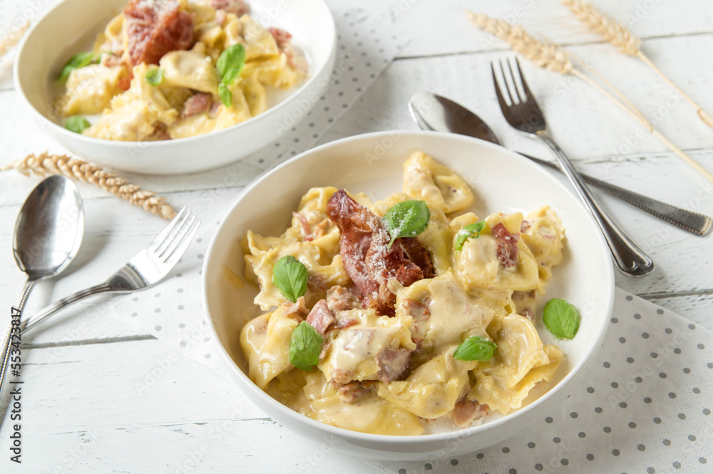 Creamy tortellini with parmesan cheese and italian ham on white background