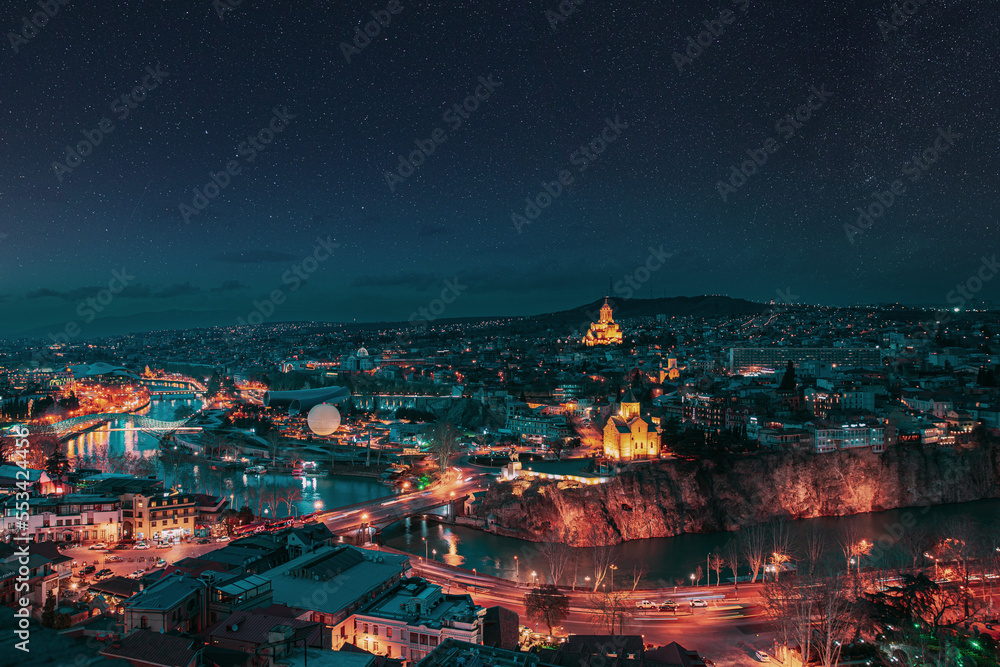Fototapeta premium Tbilisi, Georgia. night dusk evening Top View Of Famous Landmarks In spring Evening dusk night. starry sky night sky above Georgian Capital Skyline Cityscape. altered stars sky.
