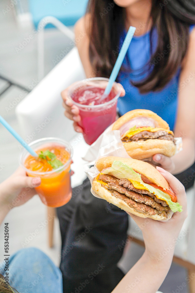Girls eating burgers and holding fruity drinks at a cafe.