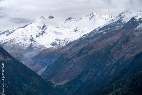 Gabler, Reichenspitze and Hahnenkamm peaks covered in snow and ice on a cloudy, rainy day of autumn. Majestic alpine peaks in the mist above Gerlos dam in Austrian Alps.