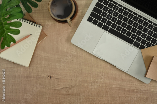 Stylish workplace with laptop computer, notepad, coffee cup and houseplant on wooden table