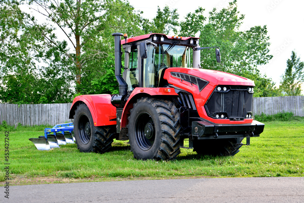 red and black agricultural tractor with big wheels isolated on green lawn with fence on background red and black agricultural tractor with big wheels isolated on green lawn with fence on background