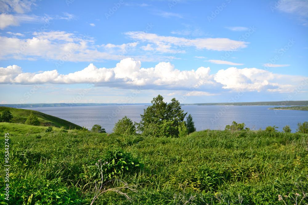 landscape with green hill and tree, river on horizon and white clouds on blue sky landscape with green hill and tree, river on horizon and white clouds on blue sky