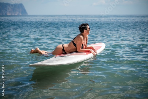 Woman sap sea. Sports girl on a surfboard in the sea on a sunny summer day. In a black bathing suit  he lies on a sap in the sea. Rest on the sea.