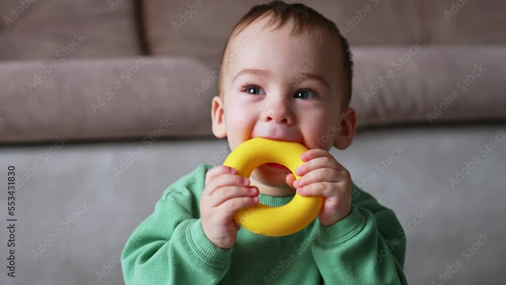 Funny cute kid tasting his plastic toys. Portrait of an adorable baby playing at home with toys. Close up. Blurred backdrop.