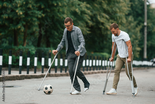 Playing soccer. Two men with crutches is outdoors on the road